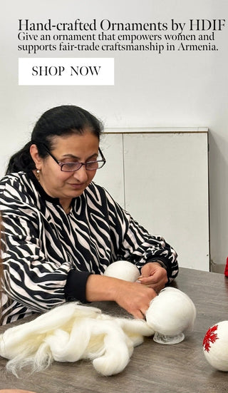 Two women working with white spherical objects on a table, with text about handcrafted ornaments and fair-trade craftsmanship.